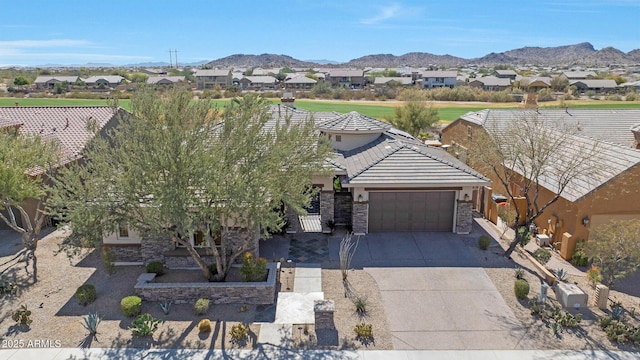 view of front facade featuring concrete driveway, stone siding, a tiled roof, an attached garage, and a mountain view