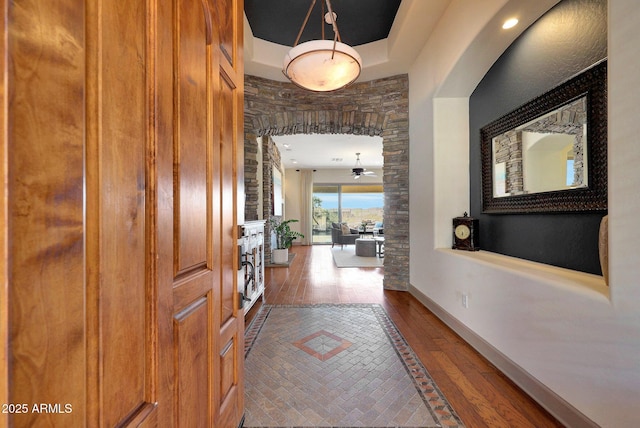 hallway featuring arched walkways, a raised ceiling, hardwood / wood-style flooring, and baseboards