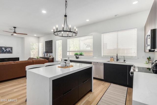 kitchen with light wood-type flooring, a kitchen island, sink, appliances with stainless steel finishes, and pendant lighting