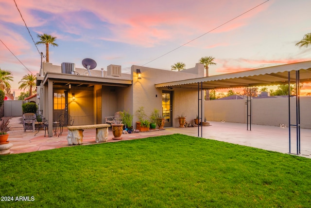 back house at dusk featuring a yard and a patio area