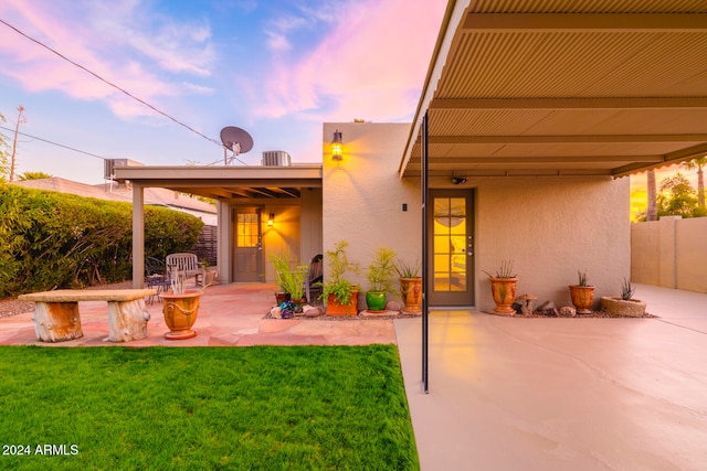 back house at dusk featuring a patio and a lawn