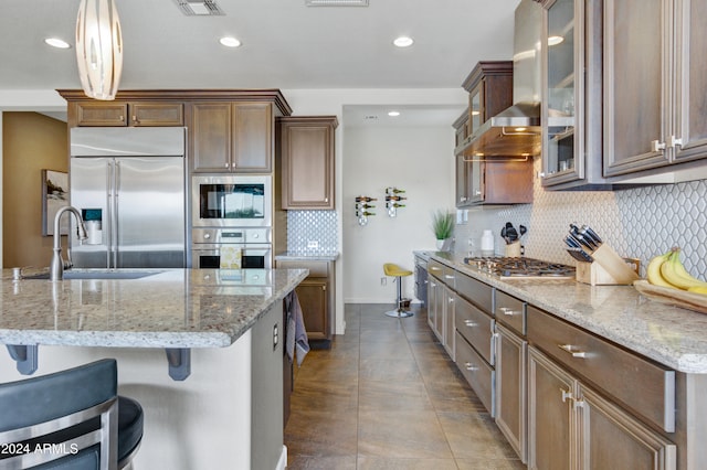 kitchen with sink, wall chimney range hood, a kitchen breakfast bar, built in appliances, and decorative light fixtures