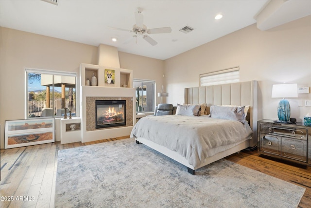 bedroom featuring hardwood / wood-style floors, a large fireplace, and ceiling fan