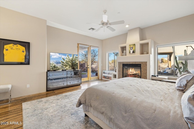 bedroom featuring wood-type flooring, a large fireplace, access to outside, and ceiling fan