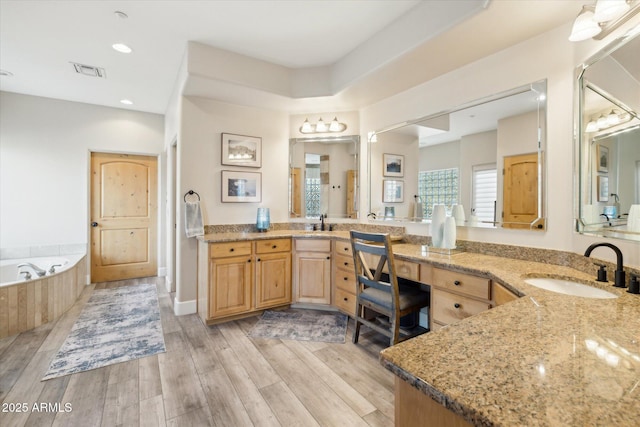 bathroom featuring hardwood / wood-style flooring, vanity, and tiled bath