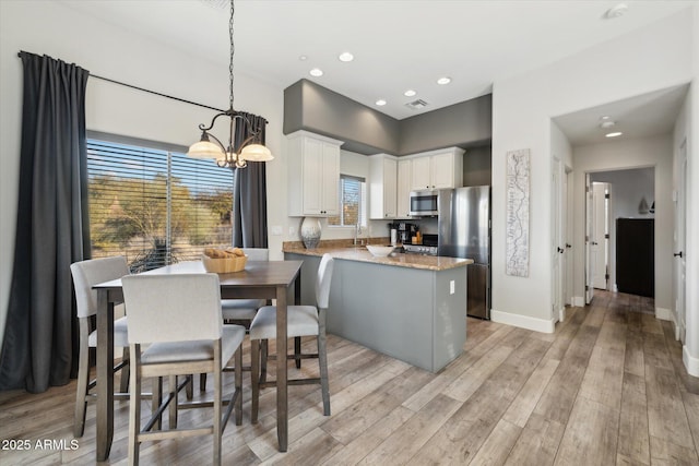 kitchen with pendant lighting, white cabinets, kitchen peninsula, stainless steel appliances, and light wood-type flooring