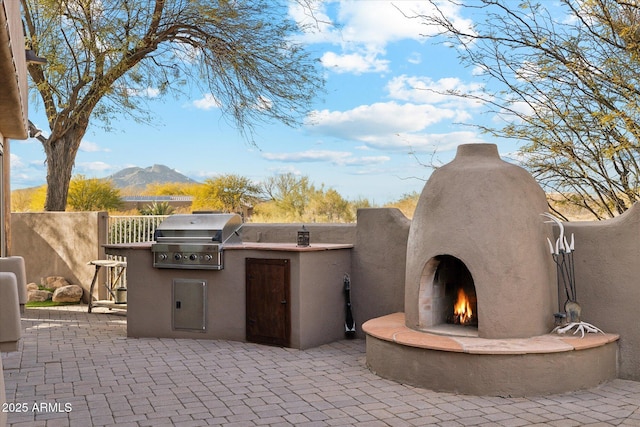 view of patio / terrace featuring area for grilling, exterior fireplace, a mountain view, and a grill