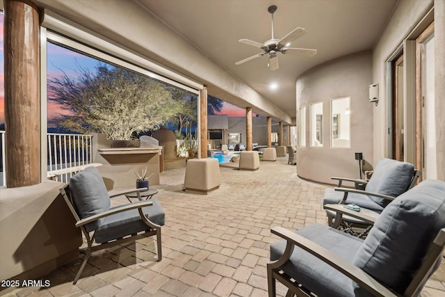 patio terrace at dusk featuring an outdoor kitchen, an outdoor hangout area, and ceiling fan