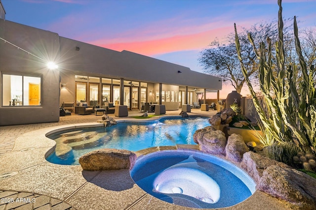 pool at dusk featuring an in ground hot tub, an outdoor hangout area, and a patio area