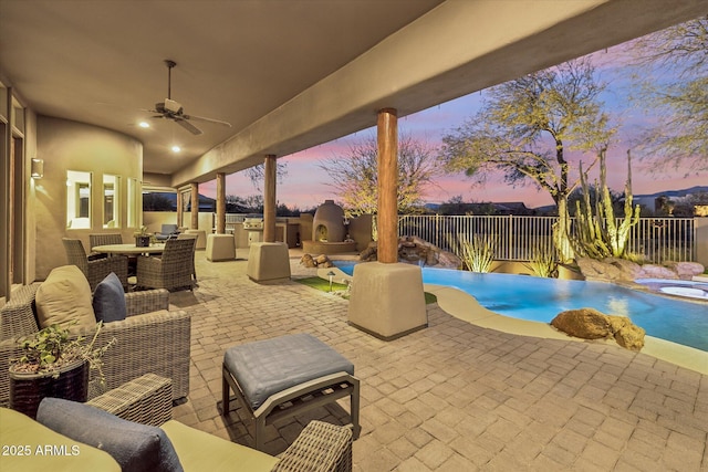 patio terrace at dusk featuring a fenced in pool, a fireplace, and ceiling fan