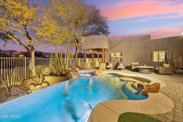 pool at dusk featuring an in ground hot tub, an outdoor hangout area, and a patio area