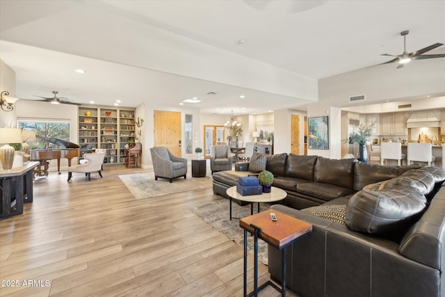 living room with ceiling fan with notable chandelier, light hardwood / wood-style floors, and built in shelves