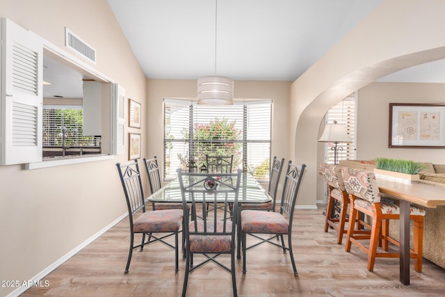 dining space featuring arched walkways, baseboards, wood finished floors, lofted ceiling, and visible vents