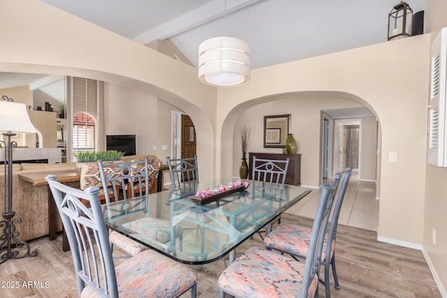 dining area with baseboards, arched walkways, lofted ceiling with beams, and wood finished floors