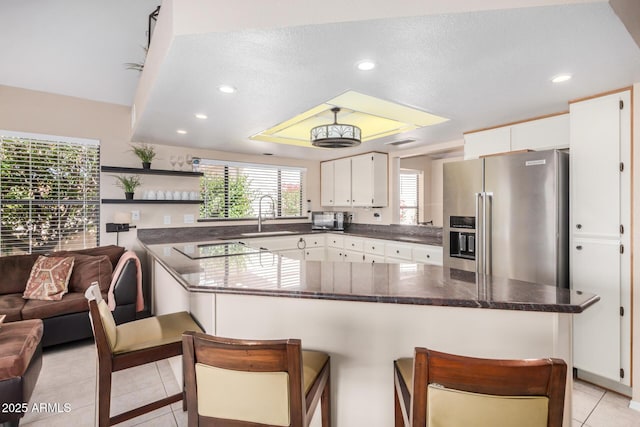kitchen featuring white cabinets, light tile patterned flooring, a sink, a kitchen breakfast bar, and stainless steel refrigerator with ice dispenser