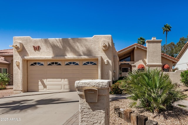 pueblo-style house featuring a garage, a chimney, driveway, and stucco siding