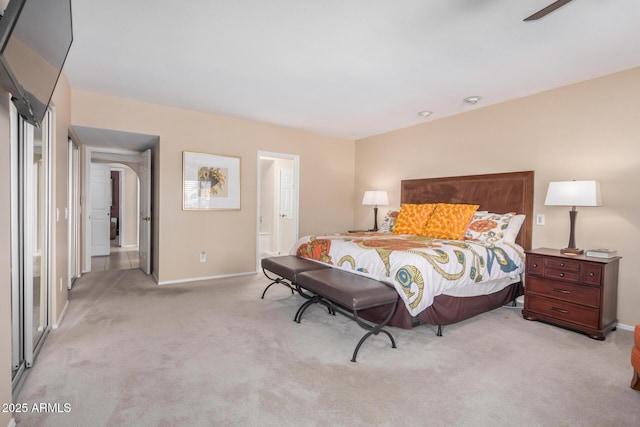 bedroom featuring baseboards, a ceiling fan, ensuite bathroom, and light carpet