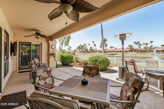view of patio with fence, a ceiling fan, outdoor dining space, and a water view