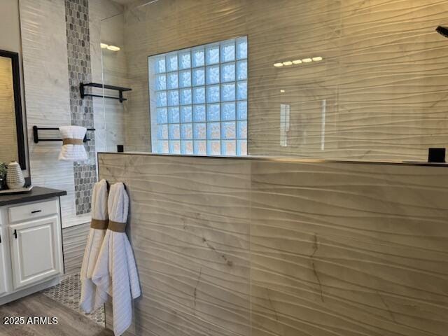 bathroom with walk in shower, vanity, and tile walls