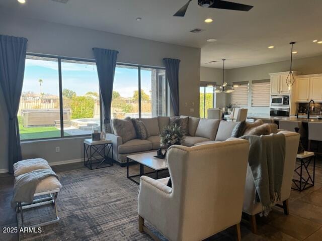 living room featuring sink and ceiling fan with notable chandelier