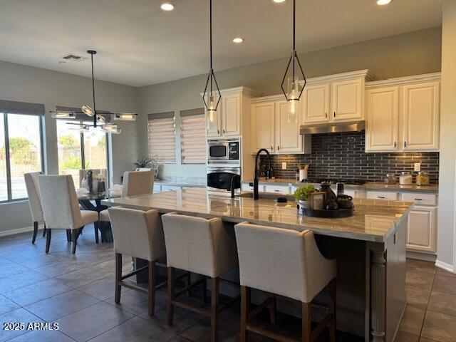 kitchen with an island with sink, appliances with stainless steel finishes, white cabinets, and decorative backsplash