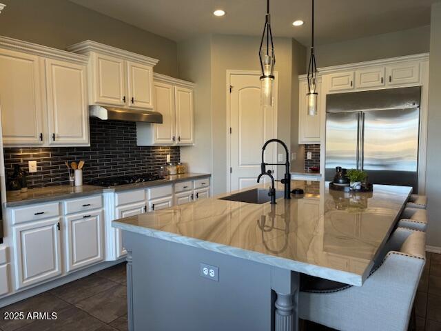 kitchen featuring white cabinetry, black gas cooktop, stainless steel built in fridge, and a center island with sink