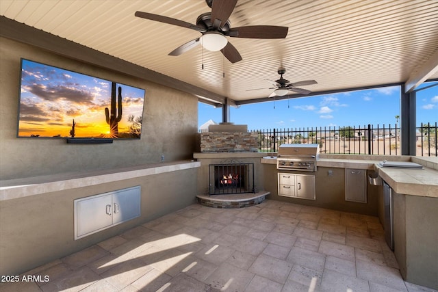 patio terrace at dusk featuring area for grilling, a grill, an outdoor stone fireplace, and ceiling fan