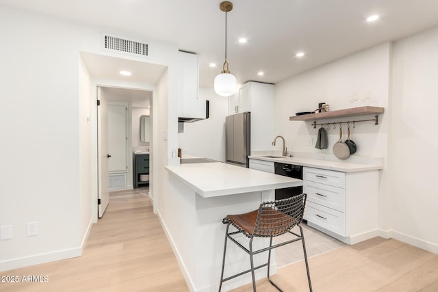 kitchen with a breakfast bar, dishwasher, white cabinetry, kitchen peninsula, and light wood-type flooring