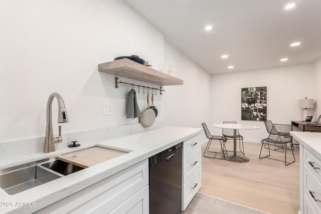 kitchen featuring sink, white cabinetry, light wood-type flooring, black dishwasher, and light stone countertops