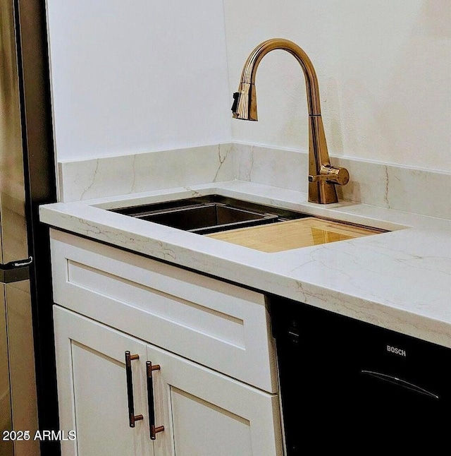 interior details with white cabinetry, black dishwasher, sink, stainless steel fridge, and light stone counters