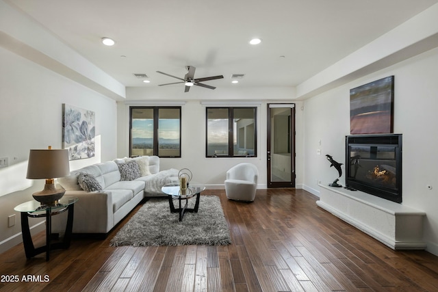 living area with a glass covered fireplace, dark wood-style flooring, visible vents, and baseboards