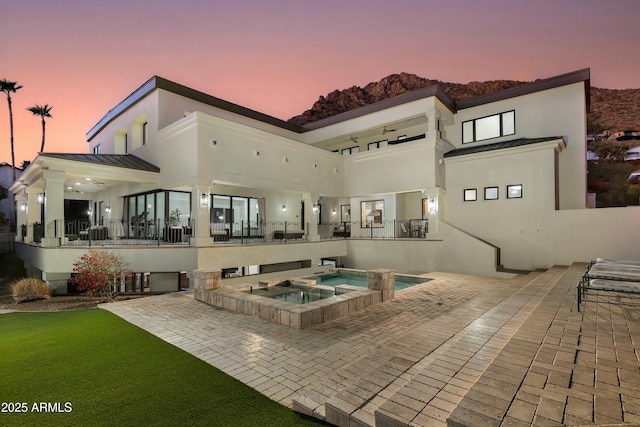 rear view of property featuring metal roof, a patio, an in ground hot tub, stucco siding, and a standing seam roof
