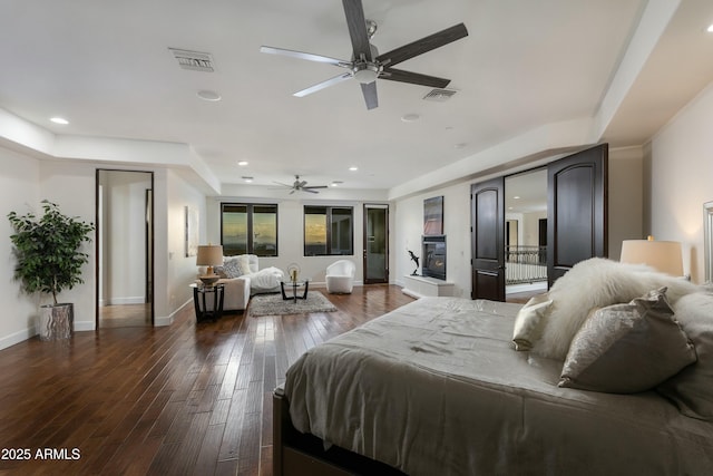 bedroom with dark wood-style floors, a glass covered fireplace, visible vents, and baseboards