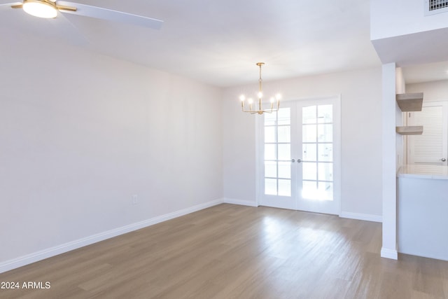 unfurnished dining area with ceiling fan with notable chandelier, wood-type flooring, and french doors