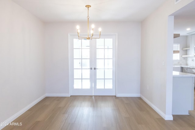 unfurnished dining area featuring a wealth of natural light, french doors, a notable chandelier, and light wood-type flooring