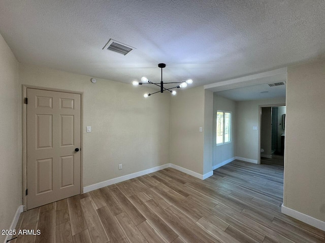 spare room featuring a textured ceiling, a notable chandelier, and light hardwood / wood-style floors