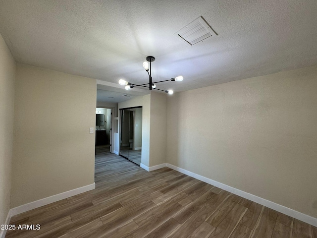 empty room featuring wood-type flooring and a chandelier