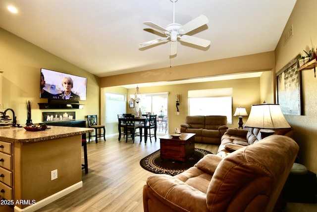 living room with lofted ceiling, sink, ceiling fan with notable chandelier, and light hardwood / wood-style floors