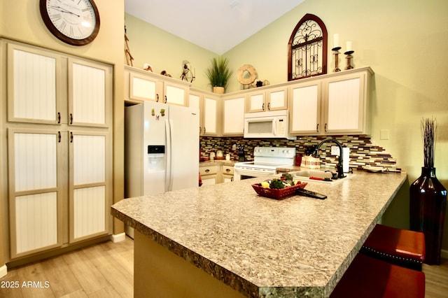 kitchen with a kitchen bar, sink, kitchen peninsula, white appliances, and decorative backsplash