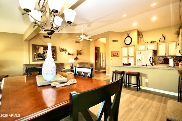 dining room with sink, ceiling fan with notable chandelier, vaulted ceiling, and light wood-type flooring