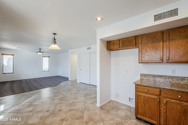 kitchen with hanging light fixtures, light tile patterned flooring, stone counters, and ceiling fan