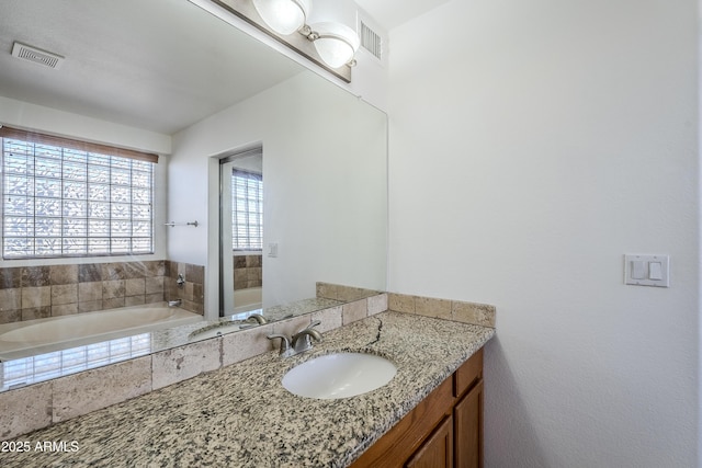 bathroom featuring a relaxing tiled tub and vanity