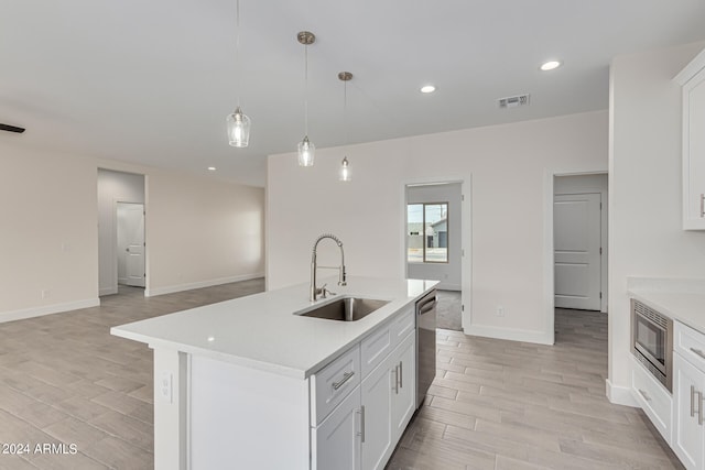 kitchen with a center island with sink, pendant lighting, white cabinetry, and sink