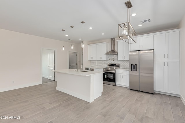 kitchen with a kitchen island with sink, stainless steel appliances, wall chimney exhaust hood, hanging light fixtures, and white cabinetry