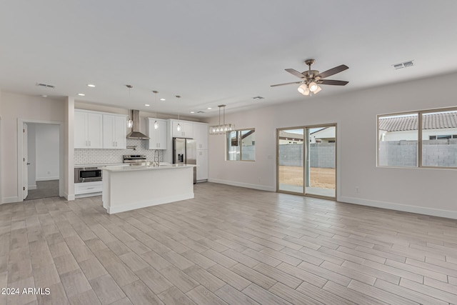 kitchen with light wood-type flooring, white cabinets, pendant lighting, wall chimney range hood, and appliances with stainless steel finishes