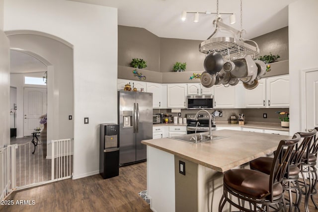 kitchen with white cabinets, appliances with stainless steel finishes, a sink, arched walkways, and high vaulted ceiling