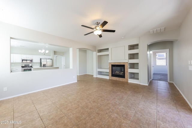 unfurnished living room with light tile patterned floors, ceiling fan with notable chandelier, a tile fireplace, and built in shelves