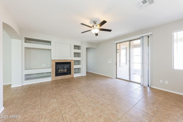 unfurnished living room with ceiling fan, light tile patterned floors, built in features, and a tile fireplace