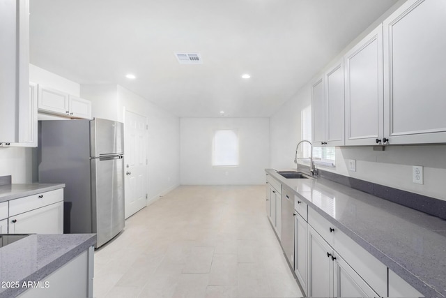 kitchen featuring stainless steel refrigerator, stone countertops, white cabinetry, and sink