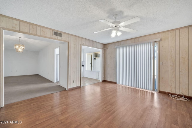 empty room featuring wooden walls, hardwood / wood-style floors, ceiling fan with notable chandelier, and a textured ceiling